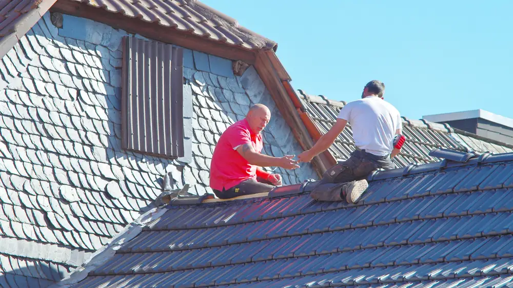 Deux couvreurs travaillant sur un toit en tuiles sous un ciel bleu